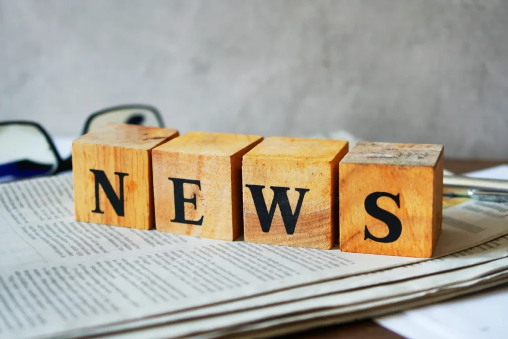 Text "NEWS" on wood cube lay on newspaper on the table.