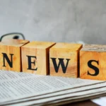 Text "NEWS" on wood cube lay on newspaper on the table.