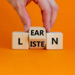 Listen and learn symbol. Businessman turns a wooden cube and changes the word 'listen' to 'learn'. Beautiful orange background, copy space. Business, education and listen and learn concept.
