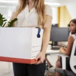 Fired female employee holding box of belongings in an office