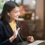 close up asian woman use earphone connect to laptop and talking greeting by video conference with friends or family at outdoor coffee restaurant in relax time , lifestyle people concept