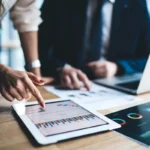 Young businessman and woman in formal sitting in office using tablet working on financial charts in workplace in company