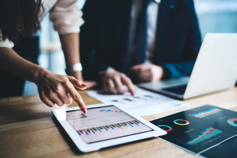 Young businessman and woman in formal sitting in office using tablet working on financial charts in workplace in company