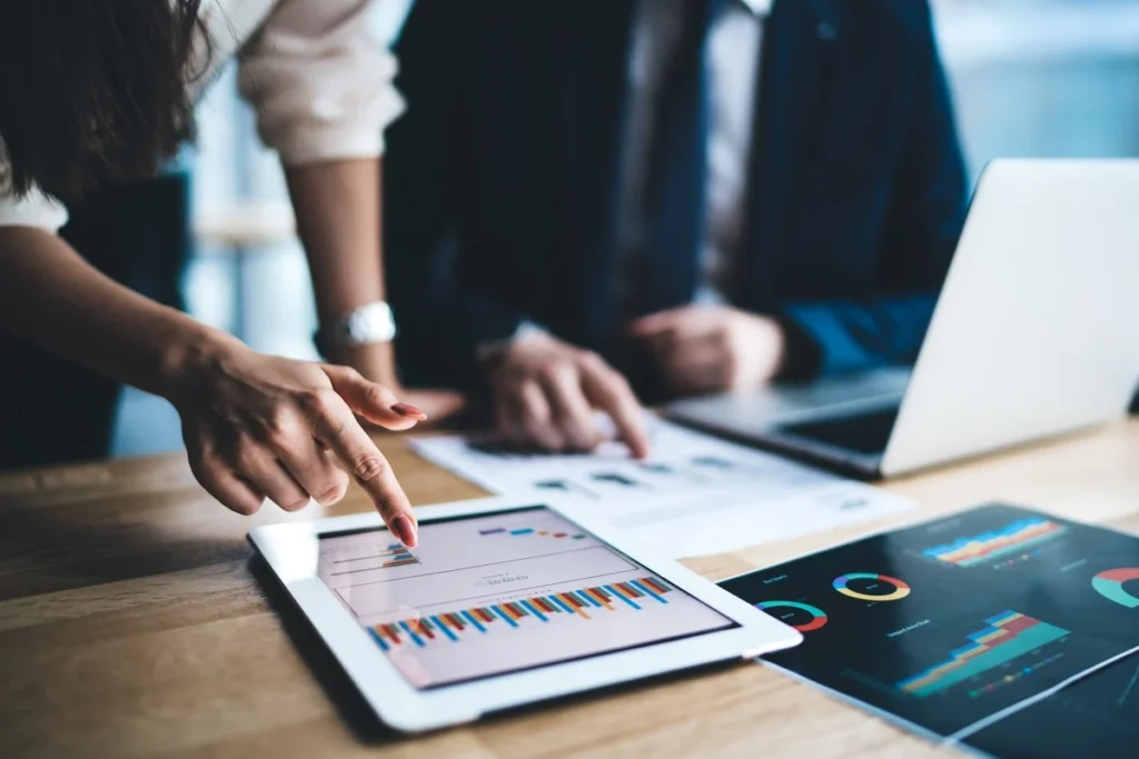 Young businessman and woman in formal sitting in office using tablet working on financial charts in workplace in company