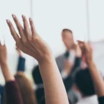 Audience raising hands up while businessman is speaking in training at the office.