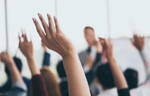 Audience raising hands up while businessman is speaking in training at the office.