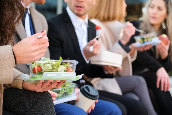 Unrecognizable businesspeople on lunch break talking while eating salad.